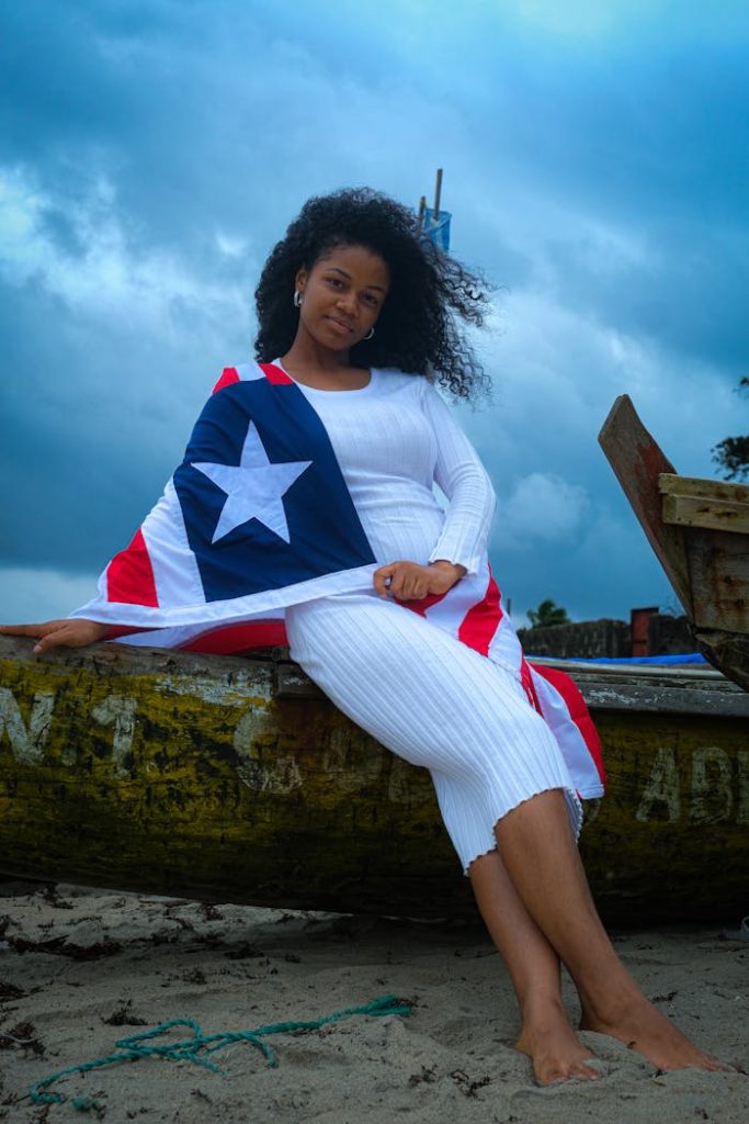girl-with-flag-28209667 A woman draped in the Liberian flag sitting on a boat at the beach.