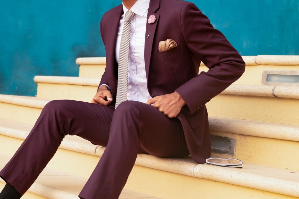 person-sitting-on-stairs-beside-sunglasses-1300550 Elegant man in a burgundy suit sitting on steps, exuding sophistication and style.